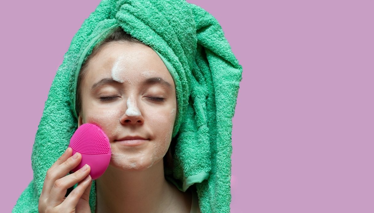ragazza ad occhi chiusi con turbante verde lava il viso con spazzola fucsia su sfondo rosa