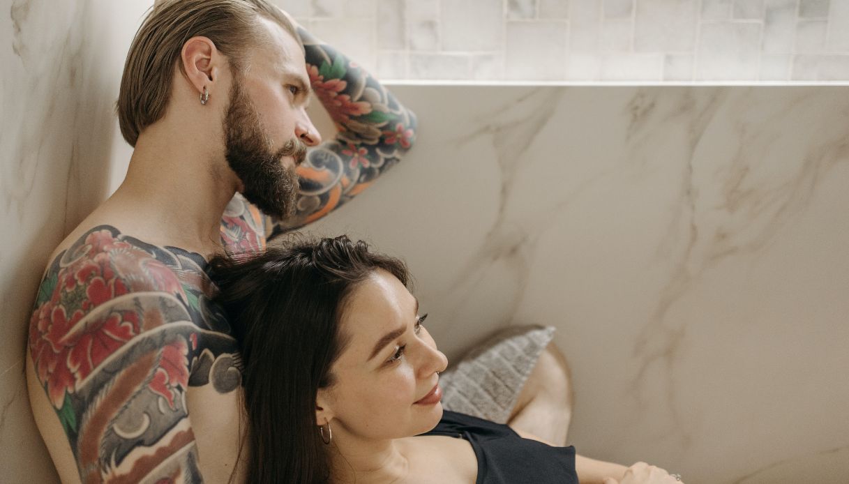 coppi abbracciata uomo con barba si tocca i capelli con braccia tatuate donna mora sorridente con maglietta nera