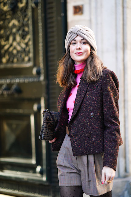 Modella con turbante beige, giacca scura, maglia rosa e pantaloni corti scuri