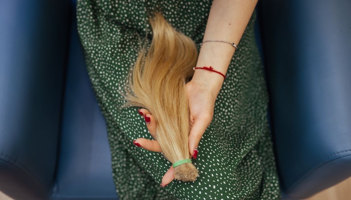ragazza con smalto rosso tiene in mano una ciocca di capelli sulle gambe coperte da un vestito verde a pois bianchi