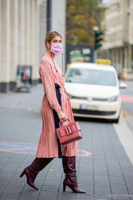 Modella con abito rosa, borsa rosa, stivali scuri e mascherina