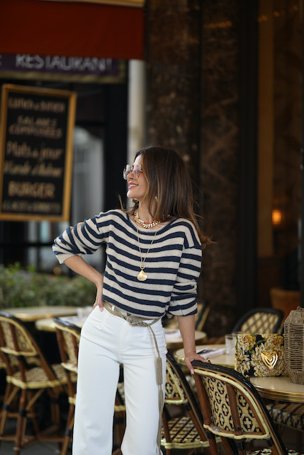 modella con maglietta a righe, jeans bianchi, occhiali da sole e collana dorata