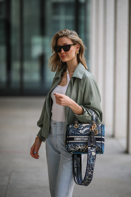 modella con giacca verde militare, maglietta bianca, jeans, borsa e collana dorata