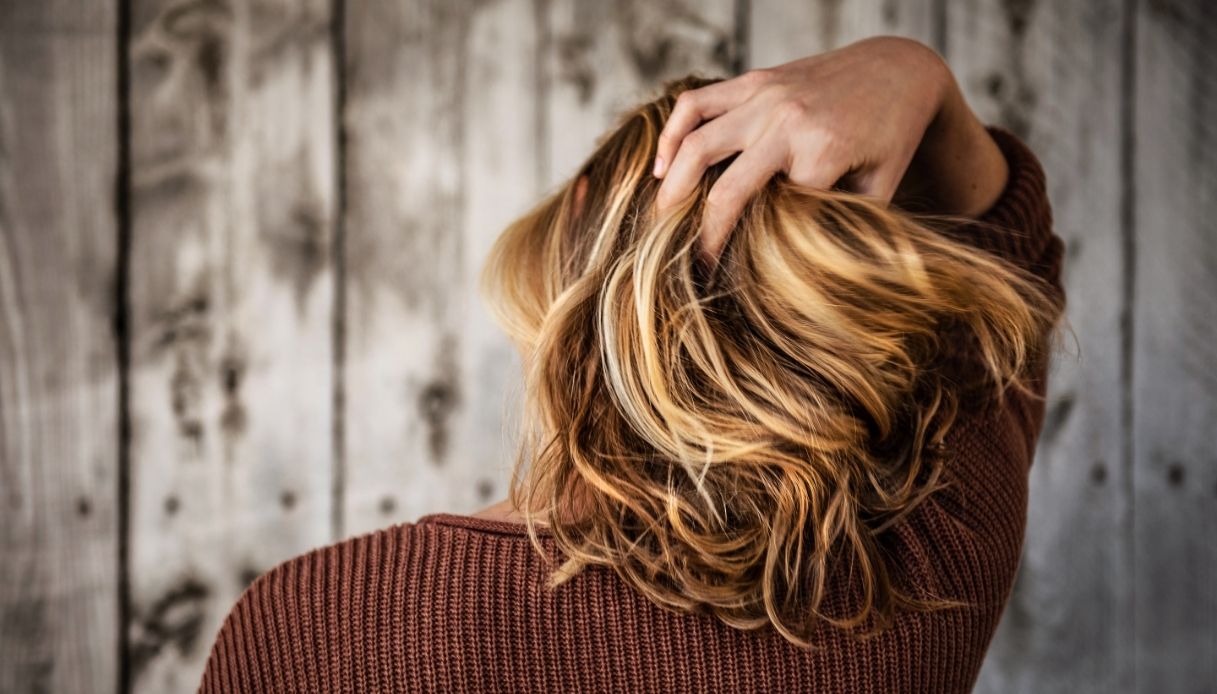 Donna si tocca i capelli biondo caramello con meches