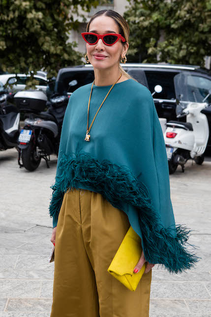 modella con maglia blu, pantaloni cachi, borsetta gialla, occhiali da sole rossi e collana dorata