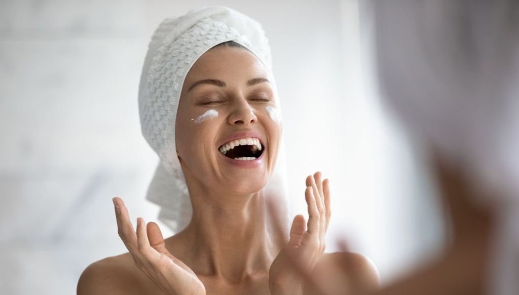 Donna con turbante che ride applica crema viso