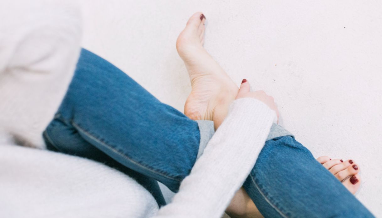 donna a gambe incrociate con blu jeans che si regge la caviglia e piedi con smalto rosso