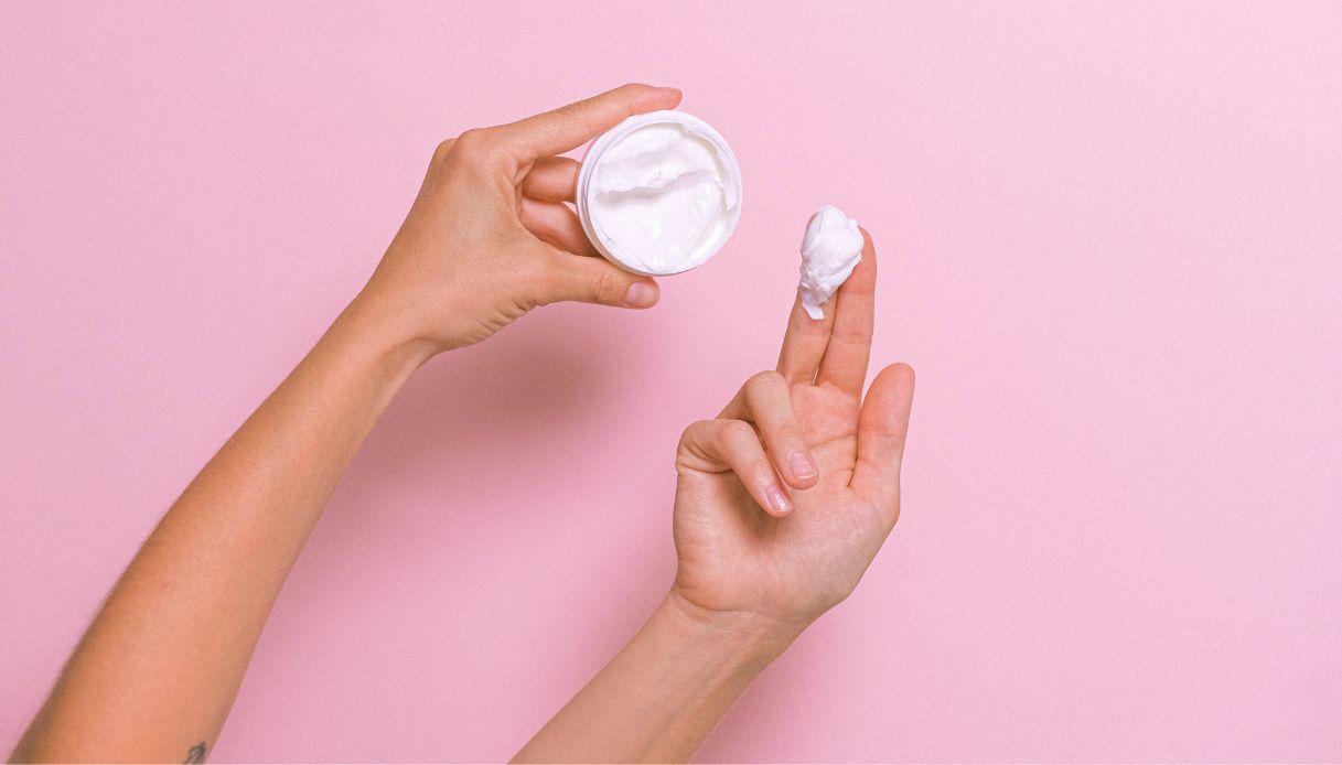 sfondo rosa mani prendono crema bianca da barattolo