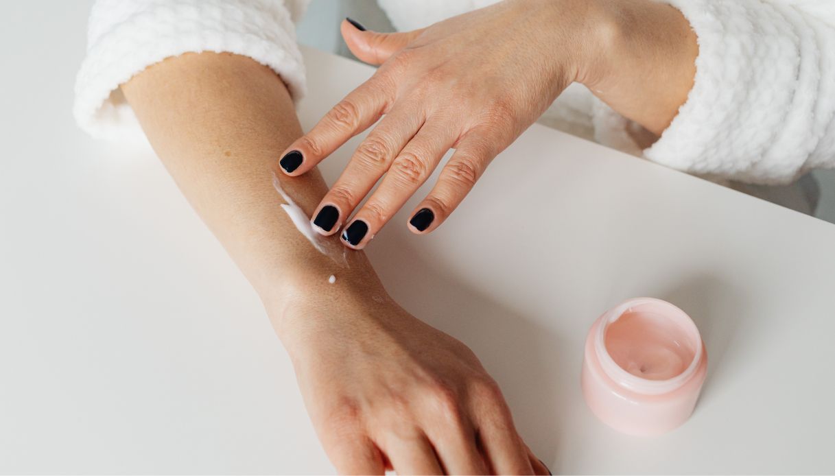 mani femminili con smalto nero stendono crema su braccio