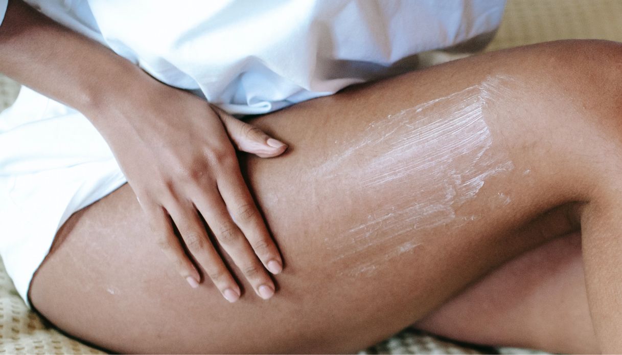 donna pelle scura stende crema su coscia con vestito bianco