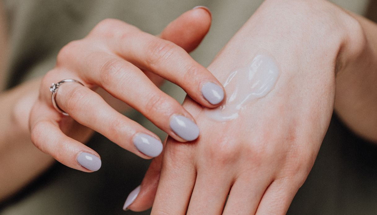 mano femminile con smalto grigio e anello stende crema fluida su mani