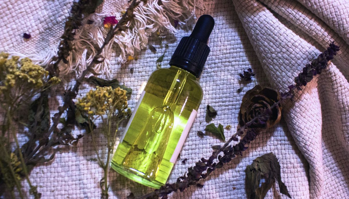 boccetta di olio verdognolo con tappo nero su sfondo viola con fiori