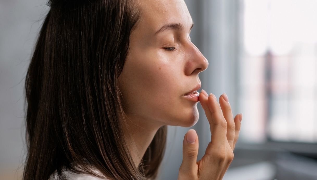 profilo di donna con capelli mori che applica qualcosa sulle labbra ad occhi chiusi