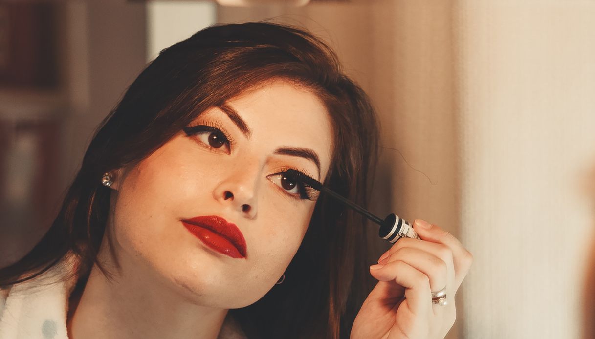 donna mora truccata applica mascara allo specchio e indossa rossetto rosso