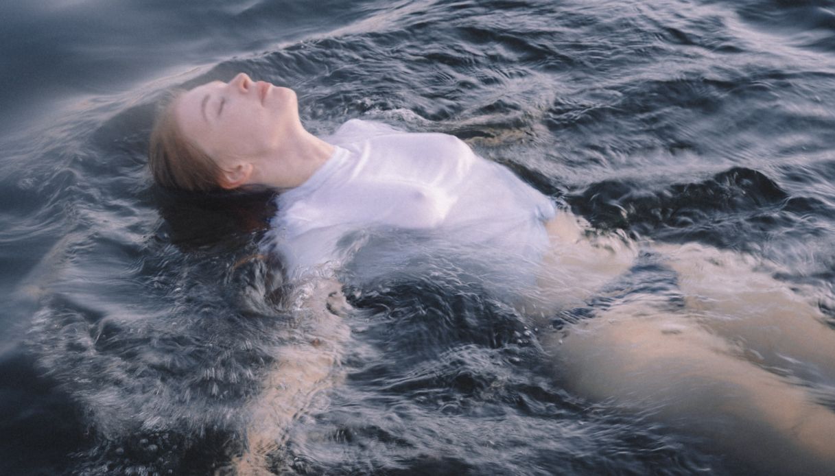 ragazza in acqua fa bagno con maglietta e mutande nere e tiene occhi chiusi