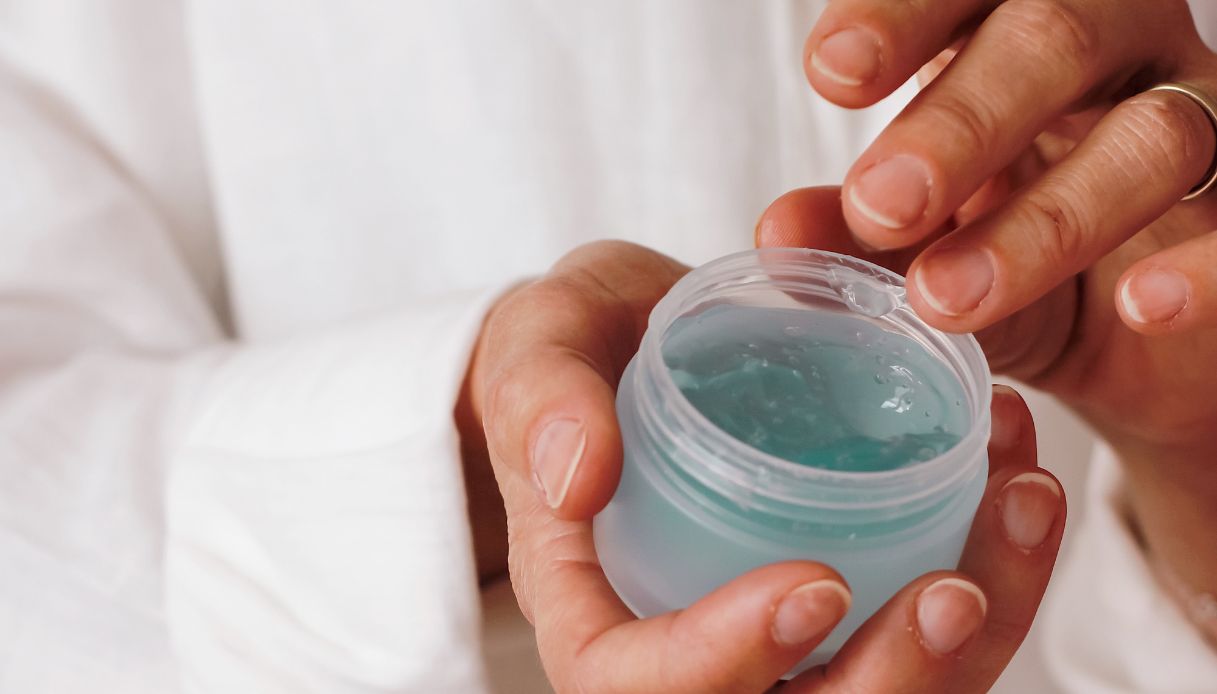 primo piano mani che prelevano crema azzurra da barattolo