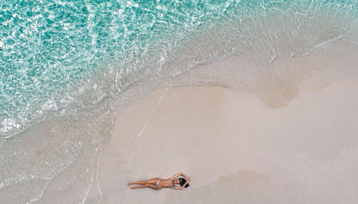 foto panoramica donna stesa sulla spiaggia con mare cristallino
