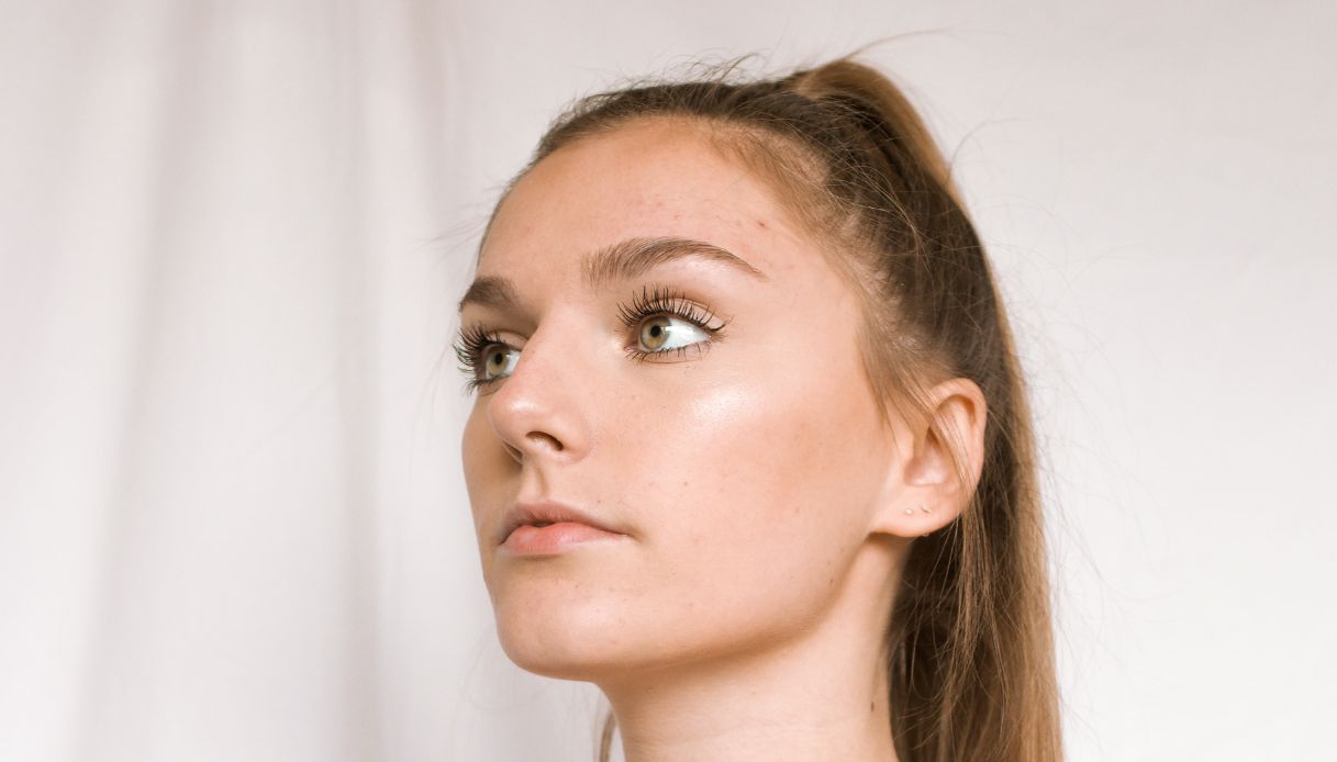ragazza con capelli raccolti in coda di cavallo su sfondo bianco ha un trucco naturale e guarda lontano verso sinistra