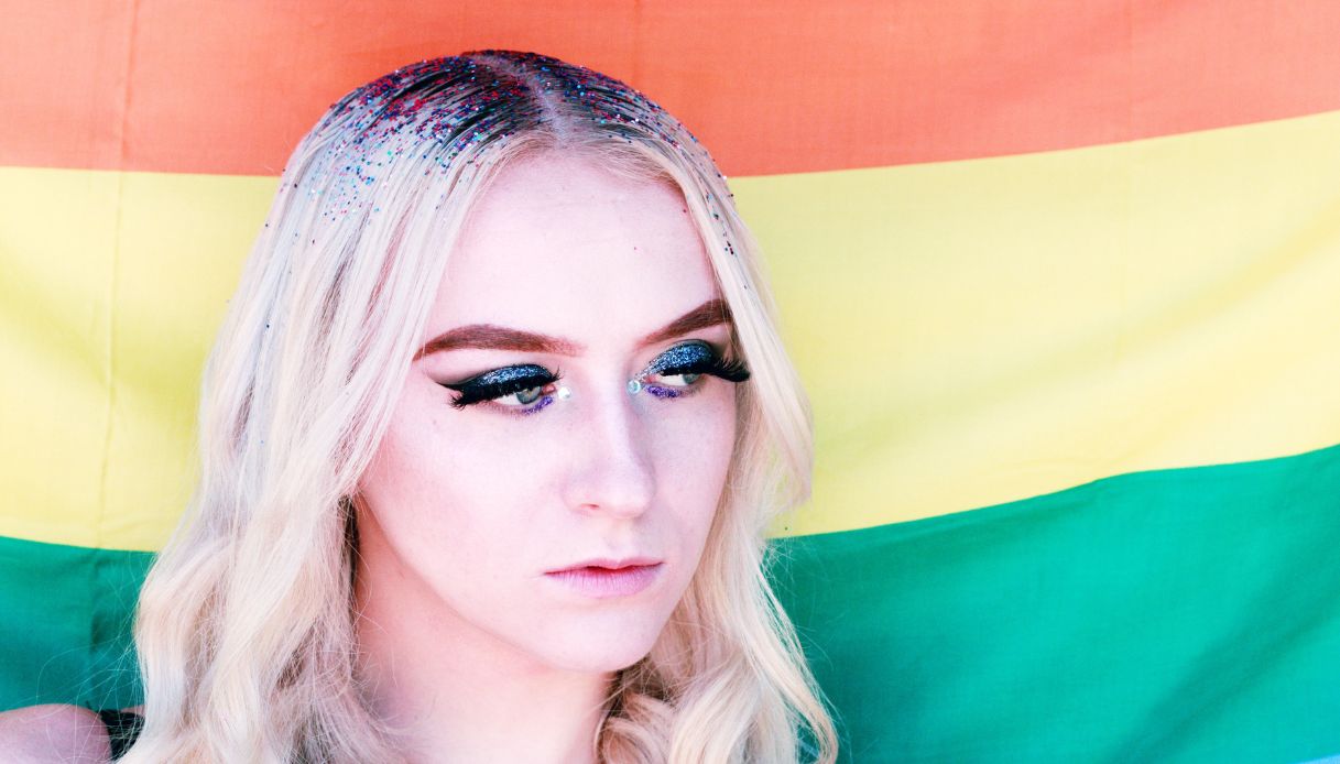 ragazza bionda con glitter sui capelli e trucco scuro su sfondo bandiera pace lgbtq+