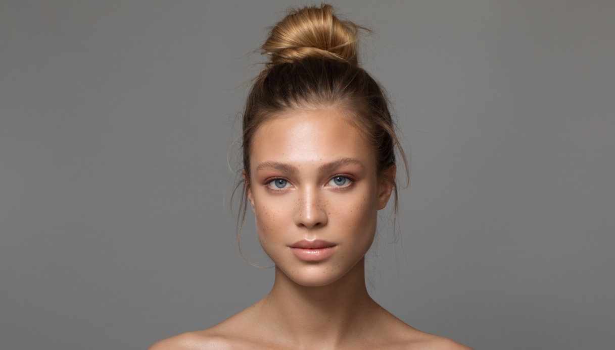 Una ragazza con i capelli biondo scuro raccolti in uno chignon alto e un makeup leggero